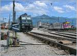 Die RTS Re 185 570-9 in Bulle, im Hintergrund verlässt ein (ex MThB) Pendelzug den Bahnhof Richtung Romont.