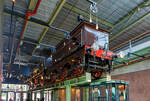 Die 1889 gebaute 2'B Schnellzug-Dampflokomotive NRS 107 „Rhijnboog“ (Rheinbogen), später HSM 353, NS 1604 (NS-Baureihe 1600), am 29 April 2025 hoch aufgeständert im Het Spoorwegmuseum (bis 2005 NSM - Nederlands Spoorwegmuseum / Niederländischen Eisenbahnmuseum) in Utrecht im ehemaligen Bahnhof Maliebaanstation.   

Die Dampflok wurde 1889 von Sharp, Stewart & Co. in Glasgow (GB) unter der Fabriknummer 3563 gebaut und an die NRS - Nederlandsche Rhijnspoorweg-Maatschappij (Niederländische Rheinbahn-Gesellschaft). Im Jahr 1890 wurde die NRS vom niederländischen Staat übernommen, der ihren Betrieb an die Staatsbahnen (SS) übertrug. Das NRS-Rollmaterial wurde zwischen den Staatsbahnen (SS) und der Hollandse IJzeren Spoorweg-Maatschappij (HSM) aufgeteilt, so wurde die NRS 107 zur HSM 353. Ab 1921, nach der Zusammenlegung des Rollmaterials der SS und der NRS, wurde die Lok zur NS 1604.

Die Baureihe NS 1600 war eine Reihe von 59 Schnellzugdampflokomotiven der NS - Nederlandse Spoorwegen (Niederländischen Eisenbahnen) und ihrer Vorgängergesellschaften, der NRS - Nederlandsche Rhijnspoorweg-Maatschappij (Niederländische Rheinbahn-Gesellschaft), der SS - Maatschappij tot Exploitatie van Staatsspoorwegen (Gesellschaft zur Nutzung der Staatseisenbahnen) und der HSM - Hollandsche IJzeren Spoorweg-Maatschappij (Niederländischen Eisenbahn-Gesellschaft). Die Loks wurden von Sharp, Stewart & Co. in Glasgow (GB) gebaut.

Die Loks vom Typ „Rhijnboog“ stellt einen großen Sprung nach vorn im Lokbau dar. Es war die erste Lokomotive, die vorne ein führendes Lauflachsen-Drehgestell hatte, das die Fahrleistung verbesserte. Dies ermöglichte auch die Länge und damit die Kapazität des Kessels zu erhöhen. Sie gehörten damals zu den größten Lokomotiven Europas.

Der Spitzname  Rhijnboog  kombiniert den Namen der niederländischen Eisenbahngesellschaft, die die Lokomotive (Nederlandsche Rhijnspoorweg-Maatschappij) mit dem Wort  Bogie  bestellt hat. Nach der Auflösung der NRS wurde die Lokserie schließlich von der HSM übernommen. Sie waren mit diesen Loks so zufrieden, dass sie 50 weitere nahezu identische Lokomotiven bestellte. Die Lokomotive NRS 107 hat einen besonderen Platz im Museum, sie überragt die Besucher von seinem erhabenen  Thron . 

NRS 101 bis 109:
Im Jahr 1889 bestellte die Nederlandsche Rhijnspoorweg-Maatschappij (NRS) neun Lokomotiven mit den Nummern 101–109 bei der Fabrik von Sharp Stewart and Company in Glasgow. Die Achsfolge der Lokomotiven war 2'B. Zum Zeitpunkt der Bestellung waren dies die ersten niederländischen Lokomotiven mit einem Laufdrehgestell vor den Antriebsrädern (Triebachsen). Sie waren die letzten von der NRS bestellten Lokomotiven. Ein Jahr später, 1890, wurde die NRS aufgelöst und die Ausrüstung zwischen der Niederländischen Eisenbahn-Gesellschaft (HSM) und der Staatlichen Eisenbahn-Ausbeutungsgesellschaft (SS) aufgeteilt. Die Lokomotiven 101, 102, 103, 108 und 109 gingen an die SS und erhielten die SS-Nummern 1101–1103 und 1108–1109. Die 104-107 gingen an das HSM und bekamen die HSM-Nummern 350-353. Da die Lokomotiven für die kleinen Drehscheiben der SS zu lang waren, übergab die SS die fünf Lokomotiven ein Jahr später, 1891, an die HSM, wo sie die Nummern 354–358 erhielten. Aufgrund des Drehgestells für die Antriebsräder, auch Bogie genannt, und der Herkunft des Rhijnspoor erhielten diese Maschinen bei der HSM den Spitznamen „Rhijnboog“.

HSM 359 bis 408:
Die HSM war mit den von ex NRS Lokomotiven so zufrieden, dass sie 40 weitere bei Sharp Stewart and Company bestellte. Diese wurden zwischen 1891 und 1892 unter den Nummern 359–398 in Dienst gestellt. Im Jahr 1900 wurde eine weitere Bestellung über 5 Einheiten mit den Nummern 399-403 bei Sharp Stewart and Company aufgegeben. Schließlich wurde im Jahr 1903 die Klasse 404–408 in Betrieb genommen, die von der North British Locomotive Company (Atlas Works) gebaut wurden, da Sharp Stewart & Co. Company inzwischen zu dieser Gesellschaft fusioniert war.

Bedingt durch den Ersten Weltkrieg wurde 1917 eine Zweckgemeinschaft der unabhängigen Eisenbahngesellschaften HSM (Hollandsche IJzeren Spoorweg-Maatschappij) und SS (Maatschappij tot Exploitatie van Staatsspoorwegen) gegründet. Die beiden Gesellschaften errichteten einen gemeinsamen Bahnbetrieb, blieben aber rechtlich unabhängig. Dies änderte sich 1938, als HIJSM und SS vollständig fusionierten und in der AG NS (Nederlandse Spoorwegen, früher Nederlandsche Spoorwegen geschrieben) aufgingen. Das Rollmaterial wurde bereits 1921 zusammengelegt, so wurden die Lok zur NS 1604 nummeriert.

Die NS 1614, 1633, 1636, 1637 und 1646 wurden 1921 mit einem Überhitzer ausgestattet. Es war beabsichtigt, die gesamte Serie damit auszurüsten, aber aufgrund enttäuschender Ergebnisse blieb es bei diesen fünf Lokomotiven. Sie wurden in den Jahren 1936–1949 außer Dienst gestellt. Die Lokomotive NS 1622 wurde als letzte dieser Baureihe im Jahr 1949 ausgemustert. Die NS 1604, ex HSM 353, ex NRS 107 „Rhijnboog“ blieb bis 1940 im Einsatz blieb. Die 1604 wurde zur Erhaltung für das Niederländische Eisenbahnmuseum in Utrecht ausgewählt und im Lokschuppen in Maastricht eingelagert, wo die Lokomotive am 8. September 1944 durch Kriegseinwirkung schwer beschädigt wurde. Nach dem Zweiten Weltkrieg wurde die Lokomotive von der NS-Hauptwerkstatt in Tilburg vollständig restauriert und in die braune Version der NRS mit der ursprünglichen Nummer 107 zurückversetzt. Seit März 1955 ist die NRS 107 im Eisenbahnmuseum ausgestellt. Nach der Sanierung des Eisenbahnmuseums in den Jahren 2003 bis 2005 wurde die Lokomotive aufgeständert.	

TECHNISCHE DATEN:
NRS-Serie: Rhijnboog, ab 1921 NS 1600
Hersteller: Sharp, Stewart & Co. in Glasgow (GB), später Atlas Works
Gebaute Anzahl: 59
Spurweite: 1.435 mm (Normalspur)
Achsfolge: 	2'B (engl. 4-4-0), gekuppelt mit dreiachsigem Tender
Länge über Puffer: 16.585 mm 
Treibraddurchmesser: 2.016 mm (neu) 
Laufraddurchmesser (Lok und Tender): 1.105 mm (neu) 
Breite: 2.222 mm
Höhe: 4.267 mm
Höchstgeschwindigkeit: 90 km/h
Rostfläche: 2,15 m²
Gesamtheizfläche: 111,6  m²
Kesselüberdruck: 10,3 kg/cm²
Anzahl der Zylinder: 2 (Ø 457 mm x 660 mm Hub)
Steuerung: Stephenson
Eigengewicht: 81,3 t (Lok 48,8 t und Tender 32,5 t) 
Anhängelast: 4.950 kg
Wasservorrat: 10,2 m³ 
Kohlevorrat: 2,8 t

