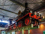 Die 1889 gebaute 2'B Schnellzug-Dampflokomotive NRS 107 „Rhijnboog“ (Rheinbogen), später HSM 353, NS 1604 (NS-Baureihe 1600), am 29 April 2025 hoch aufgeständert im Het Spoorwegmuseum (bis 2005 NSM - Nederlands Spoorwegmuseum / Niederländischen Eisenbahnmuseum) in Utrecht im ehemaligen Bahnhof Maliebaanstation.   

Die Dampflok wurde 1889 von Sharp, Stewart & Co. in Glasgow (GB) unter der Fabriknummer 3563 gebaut und an die NRS - Nederlandsche Rhijnspoorweg-Maatschappij (Niederländische Rheinbahn-Gesellschaft). Im Jahr 1890 wurde die NRS vom niederländischen Staat übernommen, der ihren Betrieb an die Staatsbahnen (SS) übertrug. Das NRS-Rollmaterial wurde zwischen den Staatsbahnen (SS) und der Hollandse IJzeren Spoorweg-Maatschappij (HSM) aufgeteilt, so wurde die NRS 107 zur HSM 353. Ab 1921, nach der Zusammenlegung des Rollmaterials der SS und der NRS, wurde die Lok zur NS 1604.

Die Baureihe NS 1600 war eine Reihe von 59 Schnellzugdampflokomotiven der NS - Nederlandse Spoorwegen (Niederländischen Eisenbahnen) und ihrer Vorgängergesellschaften, der NRS - Nederlandsche Rhijnspoorweg-Maatschappij (Niederländische Rheinbahn-Gesellschaft), der SS - Maatschappij tot Exploitatie van Staatsspoorwegen (Gesellschaft zur Nutzung der Staatseisenbahnen) und der HSM - Hollandsche IJzeren Spoorweg-Maatschappij (Niederländischen Eisenbahn-Gesellschaft). Die Loks wurden von Sharp, Stewart & Co. in Glasgow (GB) gebaut.

Die Loks vom Typ „Rhijnboog“ stellt einen großen Sprung nach vorn im Lokbau dar. Es war die erste Lokomotive, die vorne ein führendes Lauflachsen-Drehgestell hatte, das die Fahrleistung verbesserte. Dies ermöglichte auch die Länge und damit die Kapazität des Kessels zu erhöhen. Sie gehörten damals zu den größten Lokomotiven Europas.

Der Spitzname  Rhijnboog  kombiniert den Namen der niederländischen Eisenbahngesellschaft, die die Lokomotive (Nederlandsche Rhijnspoorweg-Maatschappij) mit dem Wort  Bogie  bestellt hat. Nach der Auflösung der NRS wurde die Lokserie schließlich von der HSM übernommen. Sie waren mit diesen Loks so zufrieden, dass sie 50 weitere nahezu identische Lokomotiven bestellte. Die Lokomotive NRS 107 hat einen besonderen Platz im Museum, sie überragt die Besucher von seinem erhabenen  Thron . 

NRS 101 bis 109:
Im Jahr 1889 bestellte die Nederlandsche Rhijnspoorweg-Maatschappij (NRS) neun Lokomotiven mit den Nummern 101–109 bei der Fabrik von Sharp Stewart and Company in Glasgow. Die Achsfolge der Lokomotiven war 2'B. Zum Zeitpunkt der Bestellung waren dies die ersten niederländischen Lokomotiven mit einem Laufdrehgestell vor den Antriebsrädern (Triebachsen). Sie waren die letzten von der NRS bestellten Lokomotiven. Ein Jahr später, 1890, wurde die NRS aufgelöst und die Ausrüstung zwischen der Niederländischen Eisenbahn-Gesellschaft (HSM) und der Staatlichen Eisenbahn-Ausbeutungsgesellschaft (SS) aufgeteilt. Die Lokomotiven 101, 102, 103, 108 und 109 gingen an die SS und erhielten die SS-Nummern 1101–1103 und 1108–1109. Die 104-107 gingen an das HSM und bekamen die HSM-Nummern 350-353. Da die Lokomotiven für die kleinen Drehscheiben der SS zu lang waren, übergab die SS die fünf Lokomotiven ein Jahr später, 1891, an die HSM, wo sie die Nummern 354–358 erhielten. Aufgrund des Drehgestells für die Antriebsräder, auch Bogie genannt, und der Herkunft des Rhijnspoor erhielten diese Maschinen bei der HSM den Spitznamen „Rhijnboog“.

HSM 359 bis 408:
Die HSM war mit den von ex NRS Lokomotiven so zufrieden, dass sie 40 weitere bei Sharp Stewart and Company bestellte. Diese wurden zwischen 1891 und 1892 unter den Nummern 359–398 in Dienst gestellt. Im Jahr 1900 wurde eine weitere Bestellung über 5 Einheiten mit den Nummern 399-403 bei Sharp Stewart and Company aufgegeben. Schließlich wurde im Jahr 1903 die Klasse 404–408 in Betrieb genommen, die von der North British Locomotive Company (Atlas Works) gebaut wurden, da Sharp Stewart & Co. Company inzwischen zu dieser Gesellschaft fusioniert war.

Bedingt durch den Ersten Weltkrieg wurde 1917 eine Zweckgemeinschaft der unabhängigen Eisenbahngesellschaften HSM (Hollandsche IJzeren Spoorweg-Maatschappij) und SS (Maatschappij tot Exploitatie van Staatsspoorwegen) gegründet. Die beiden Gesellschaften errichteten einen gemeinsamen Bahnbetrieb, blieben aber rechtlich unabhängig. Dies änderte sich 1938, als HIJSM und SS vollständig fusionierten und in der AG NS (Nederlandse Spoorwegen, früher Nederlandsche Spoorwegen geschrieben) aufgingen. Das Rollmaterial wurde bereits 1921 zusammengelegt, so wurden die Lok zur NS 1604 nummeriert.

Die NS 1614, 1633, 1636, 1637 und 1646 wurden 1921 mit einem Überhitzer ausgestattet. Es war beabsichtigt, die gesamte Serie damit auszurüsten, aber aufgrund enttäuschender Ergebnisse blieb es bei diesen fünf Lokomotiven. Sie wurden in den Jahren 1936–1949 außer Dienst gestellt. Die Lokomotive NS 1622 wurde als letzte dieser Baureihe im Jahr 1949 ausgemustert. Die NS 1604, ex HSM 353, ex NRS 107 „Rhijnboog“ blieb bis 1940 im Einsatz blieb. Die 1604 wurde zur Erhaltung für das Niederländische Eisenbahnmuseum in Utrecht ausgewählt und im Lokschuppen in Maastricht eingelagert, wo die Lokomotive am 8. September 1944 durch Kriegseinwirkung schwer beschädigt wurde. Nach dem Zweiten Weltkrieg wurde die Lokomotive von der NS-Hauptwerkstatt in Tilburg vollständig restauriert und in die braune Version der NRS mit der ursprünglichen Nummer 107 zurückversetzt. Seit März 1955 ist die NRS 107 im Eisenbahnmuseum ausgestellt. Nach der Sanierung des Eisenbahnmuseums in den Jahren 2003 bis 2005 wurde die Lokomotive aufgeständert.	

TECHNISCHE DATEN:
NRS-Serie: Rhijnboog, ab 1921 NS 1600
Hersteller: Sharp, Stewart & Co. in Glasgow (GB), später Atlas Works
Gebaute Anzahl: 59
Spurweite: 1.435 mm (Normalspur)
Achsfolge: 	2'B (engl. 4-4-0), gekuppelt mit dreiachsigem Tender
Länge über Puffer: 16.585 mm 
Treibraddurchmesser: 2.016 mm (neu) 
Laufraddurchmesser (Lok und Tender): 1.105 mm (neu) 
Breite: 2.222 mm
Höhe: 4.267 mm
Höchstgeschwindigkeit: 90 km/h
Rostfläche: 2,15 m²
Gesamtheizfläche: 111,6  m²
Kesselüberdruck: 10,3 kg/cm²
Anzahl der Zylinder: 2 (Ø 457 mm x 660 mm Hub)
Steuerung: Stephenson
Eigengewicht: 81,3 t (Lok 48,8 t und Tender 32,5 t) 
Anhängelast: 4.950 kg
Wasservorrat: 10,2 m³ 
Kohlevorrat: 2,8 t
